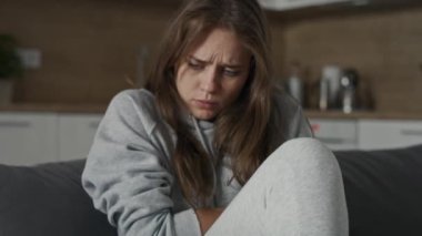 İştahsız, beyaz bir kadın kanepesinde büyük bir ağrı ile oturuyor. 8K 'da kırmızı helyum kamerayla çekildi..   