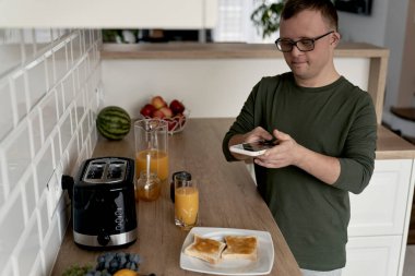 Down sendromlu beyaz bir adam kahvaltı hazırlarken fotoğrafını çekiyor.