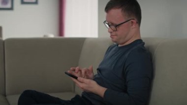 Evdeki koltukta otururken cep telefonu kullanan Down sendromlu bir adam. 8K 'da kırmızı helyum kamerayla çekildi..  