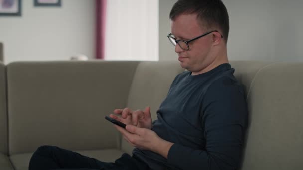 Mężczyzna Zespołem Downa Korzystający Telefonu Komórkowego Domu Podczas Siedzenia Kanapie — Wideo stockowe