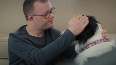 Down sendromlu beyaz bir adam yerde oturup evcil köpekle oynuyor. 8K 'da kırmızı helyum kamerayla çekildi..   