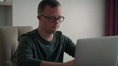 Evde dizüstü bilgisayar kullanarak, Down sendromlu yetişkin bir beyaz adama odaklan. 8K 'da kırmızı helyum kamerayla çekildi..     