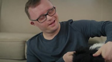 Down sendromlu beyaz bir adam yerde oturup evcil köpekle oynuyor. 8K 'da kırmızı helyum kamerayla çekildi..     
