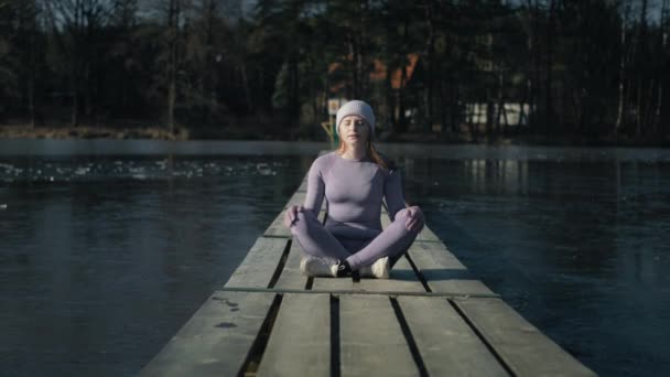 桟橋に座っている白人女性の外にズームし 冬に目を閉じて瞑想 8Kでレッドヘリウムカメラで撮影 — ストック動画
