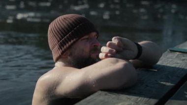 Kafkasyalı yetişkin bir adam donmuş gölde yüzerken akıllı adam parametrelerini kontrol ediyor. 8K 'da kırmızı helyum kamerayla çekildi.. 