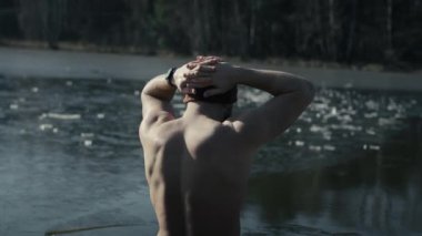 Beyaz yetişkin bir adam kışın iskeleden yavaşça donmuş bir göle giriyor. 8K 'da kırmızı helyum kamerayla çekildi.. 