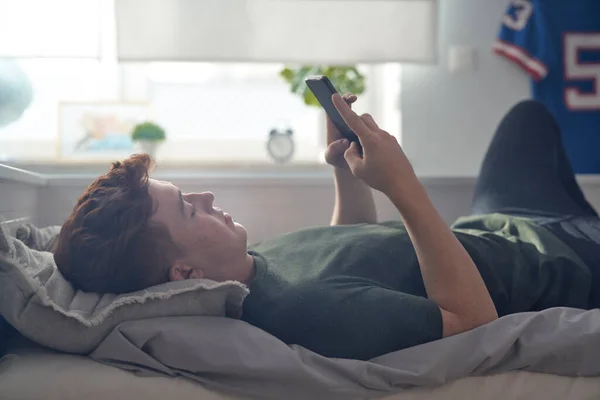 Blank Tiener Jongen Browsen Telefoon Terwijl Liggend Bed Zijn Rug — Stockfoto