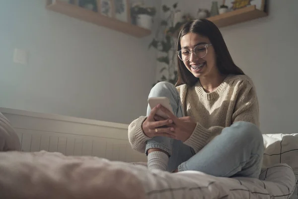 Vit Tonåring Flicka Bläddrar Telefon Och Ler Medan Sitter Sängen — Stockfoto