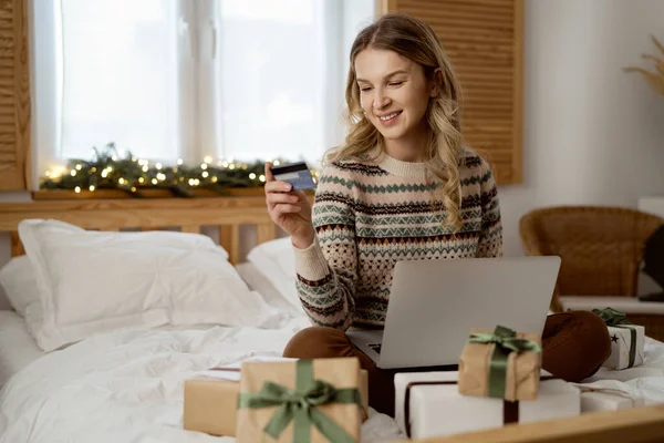 白人女性のベッドに座って ラップトップとクレジットカードの使用でクリスマスショッピングを行う — ストック写真