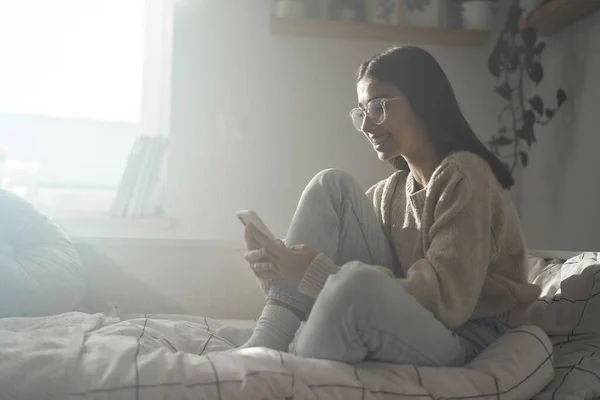 Vit Tonåring Flicka Bläddrar Telefon Och Ler Medan Sitter Sängen — Stockfoto