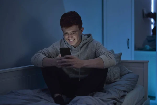 Vidám Kaukázusi Tinédzser Fiú Mobiltelefont Használ Miközben Éjjel Szobájában — Stock Fotó