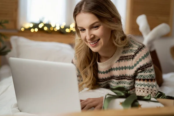 白人女性は前にベッドに横たわって クリスマスプレゼントの間にノートパソコンを閲覧 — ストック写真