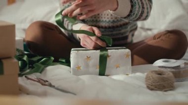 Tanımlanamayan beyaz bir kadının yatakta oturması ve evde Noel hediyesi paketlemesi. 8K 'da kırmızı helyum kamerayla çekildi..   