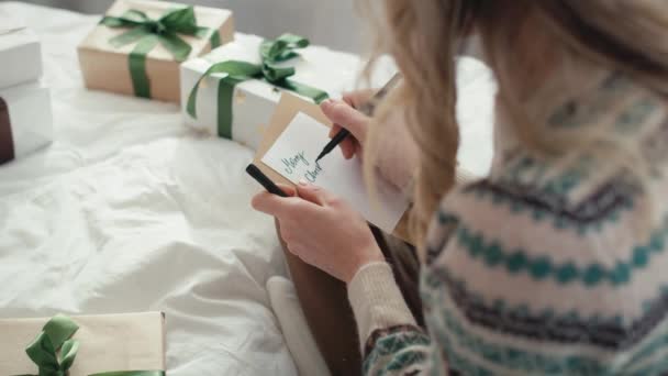 ベッドの上に座って 包まれた本のためのクリスマスカードを書いている白人女性のトップビュー 8Kでレッドヘリウムカメラで撮影 — ストック動画