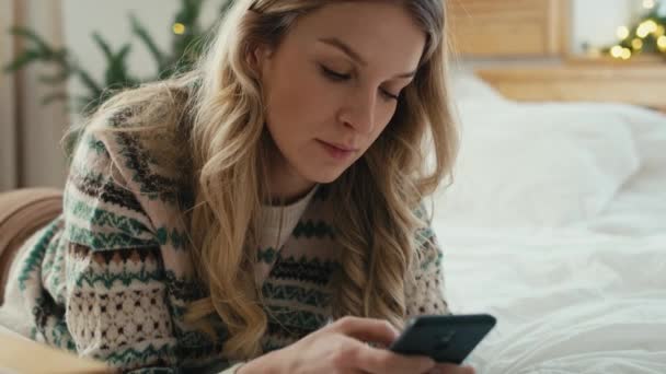 Mulher Caucasiana Usando Telefone Enquanto Deitada Frente Cama Época Natal — Vídeo de Stock