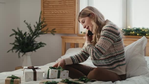 Valkoihoinen Nainen Käärimässä Joululahjaa Puhumassa Puhelimessa Istuessaan Sängyssä Laukaus Punaisella — kuvapankkivideo