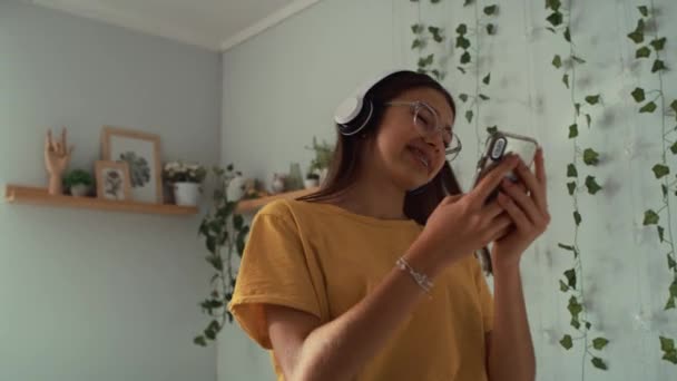 白人の10代の少女がヘッドフォンと電話で彼女の部屋で踊ります 8Kでレッドヘリウムカメラで撮影 — ストック動画