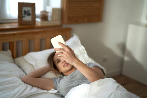 白种人女人早上用手机躺在床上 — 图库照片