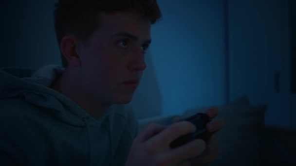 夜にゲームコントローラーで遊ぶ白人の十代の少年に焦点を当てます 8Kでレッドヘリウムカメラで撮影 — ストック動画