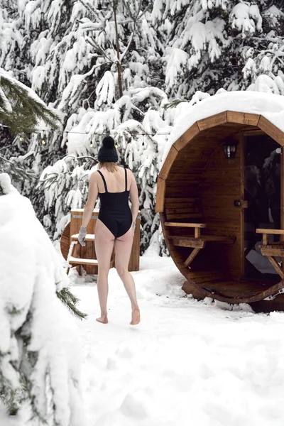 Caucasian woman going into the barrel with cold water in winter outdoors