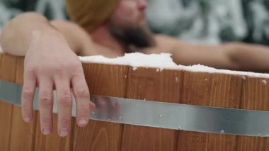 Caucasian man sitting in wooden barrel with frozen water. Shot with RED helium camera in 8K.    