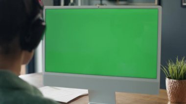 Rear view of woman working on computer with green screen. Shot with RED helium camera in 8K.