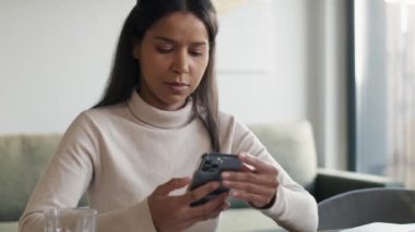 Mixed race woman sitting at the desk and browsing phone. Shot with RED helium camera in 8K.  