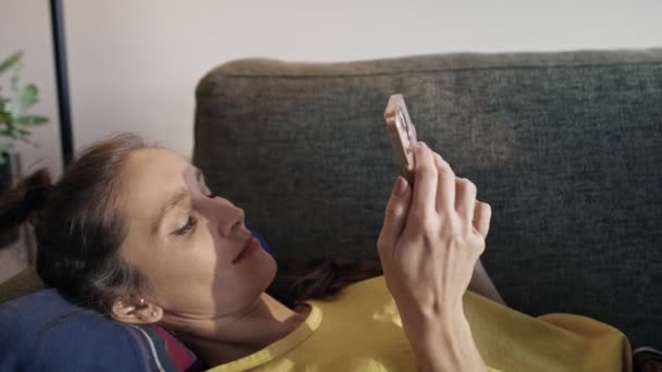 白人女性はソファに横になり 電話を閲覧する 8Kでレッドヘリウムカメラで撮影 — ストック動画
