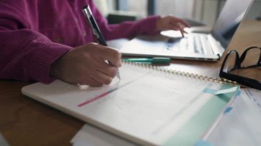 Unrecognizable woman working on computer and making notes at home. Shot with RED helium camera in 8K.    
