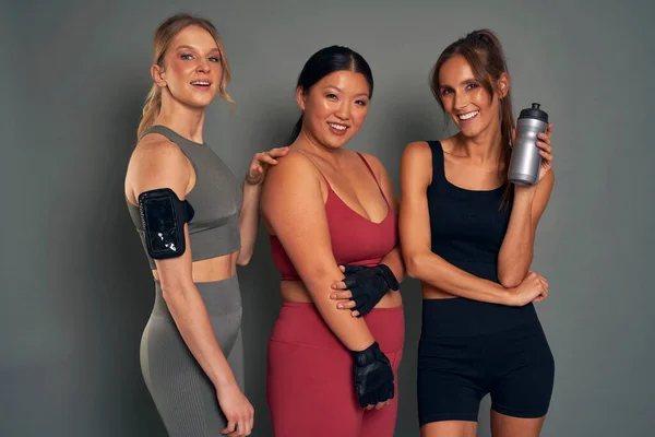 Three young women in sports clothes and gym accessories in studio shot