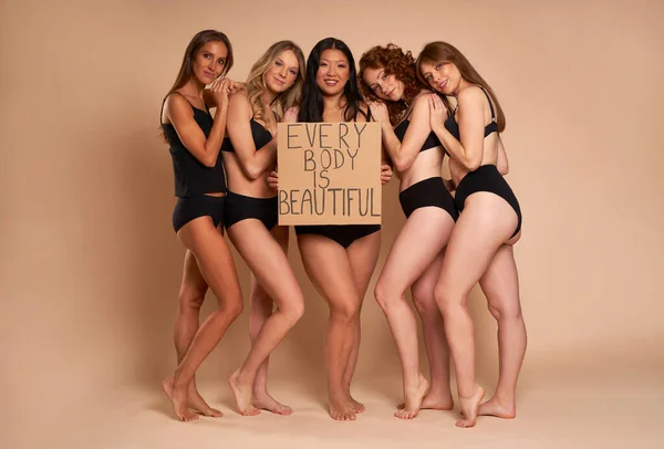 Group of women in underwear looking at camera and holding banner