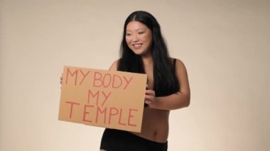 Smiling plus size woman in black underwear dancing in the studio and holding a banner. Shot with RED helium camera in 8K. 