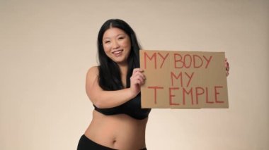 Smiling plus size woman in black underwear dancing in the studio and holding a banner. Shot with RED helium camera in 8K. 