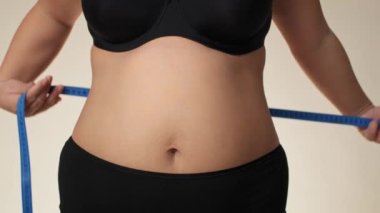 Unrecognizable plus size woman in underwear taking measure of her waist with measuring tape. Shot with RED helium camera in 8K. 