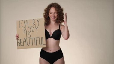 Cheerful caucasian red head woman in underwear in the studio holding a banner. Shot with RED helium camera in 8K. 