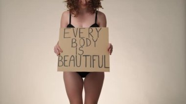 Cheerful caucasian red head woman in underwear in the studio holding a banner. Shot with RED helium camera in 8K.