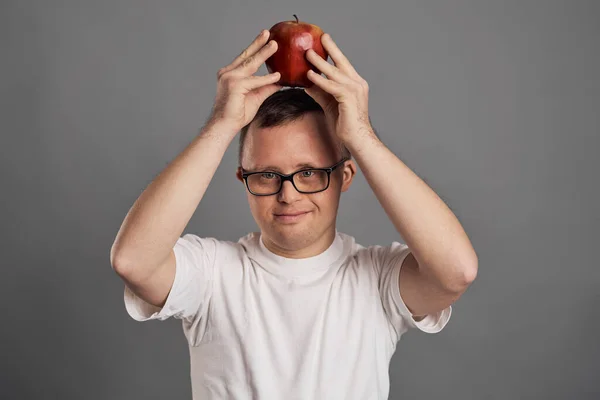 Man with down syndrome holding apple below on head on gray background