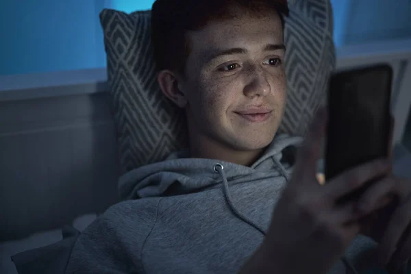 Vidám Kaukázusi Tinédzser Fiú Mobiltelefont Használ Miközben Éjjel Ágyban Fekszik — Stock Fotó