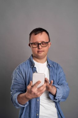 Adult man with down syndrome using mobile phone on gray background