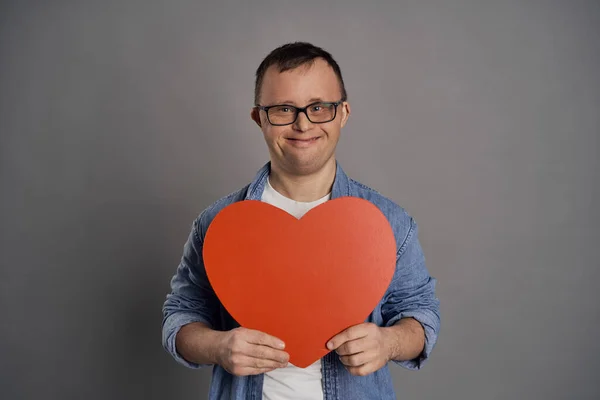 Kavkazský Muž Downovým Syndromem Drží Velké Červené Srdce Šedém Pozadí — Stock fotografie