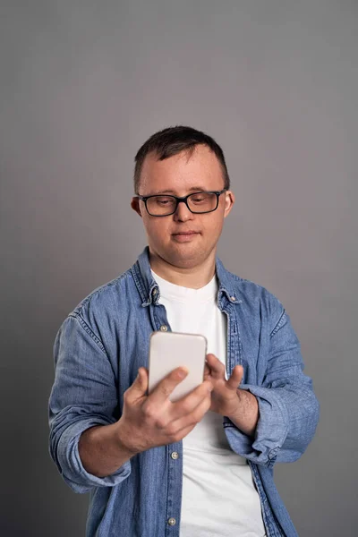 Dospělý Muž Downovým Syndromem Pomocí Mobilního Telefonu Šedém Pozadí — Stock fotografie