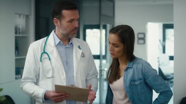 保健所の廊下で文書を議論白人男性医師と女性患者 8Kでレッドヘリウムカメラで撮影 — ストック動画