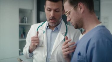 İki ciddi Kafkas erkek doktor klinikte dokümanlar üzerinde tartışıyorlar. 8K 'da kırmızı helyum kamerayla çekildi..