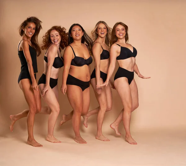 Group of cheerful women in black underwear standing and smiling towards the camera