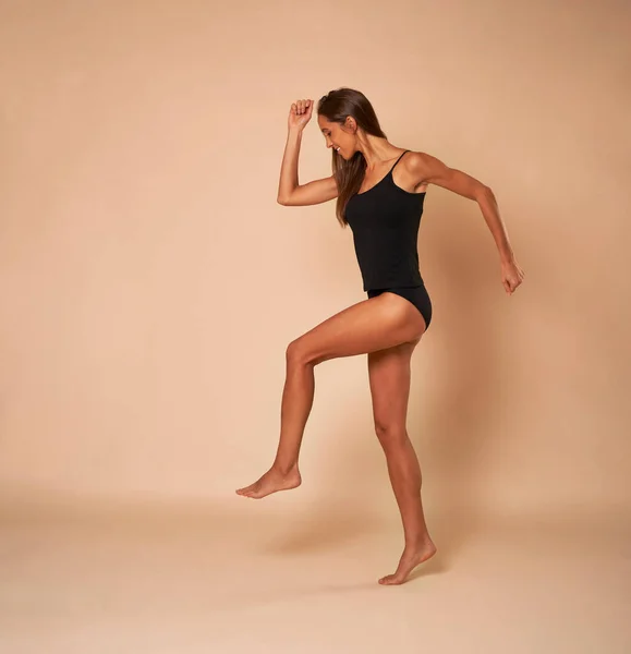 Side view of skinny woman in black underwear walking on nude background