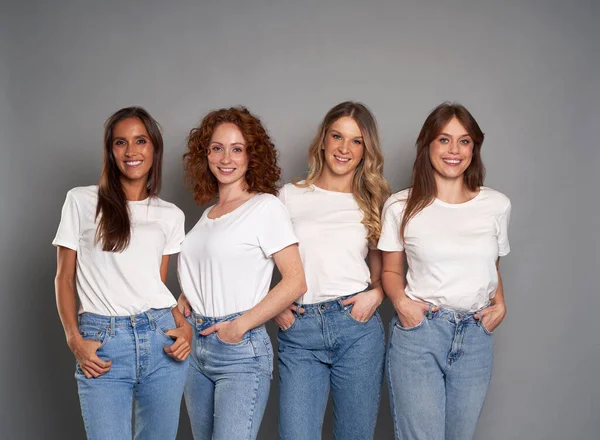 4人の若い白人女性が青いジーンズと白いTシャツを着て灰色の背景 — ストック写真