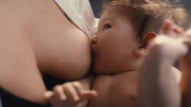 Annesi tarafından emzirilen ve bacaklarıyla oynayan Asyalı bebeğe yakın çekim. 8K 'da kırmızı helyum kamerayla çekildi..  