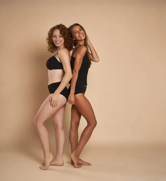 两个身穿黑色内裤的女人背靠背站在镜头前微笑 — 图库照片
