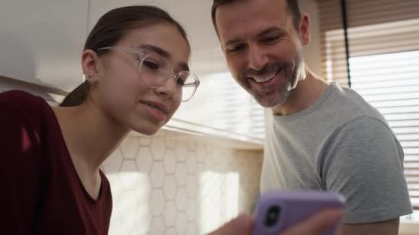 調理中に台所で携帯電話を見て10代の娘を持つ白人の父親 8Kでレッドヘリウムカメラで撮影 — ストック動画