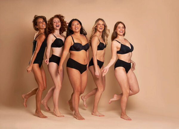 Group of cheerful women in black underwear standing and smiling towards the camera